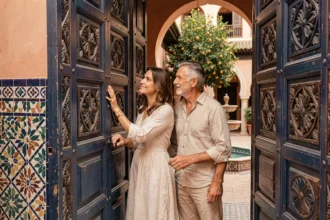 Couple visitant l'entrée d'une villa traditionnelle marocaine à Marrakech avec des portes en cèdre sculpté et des carreaux de zellige