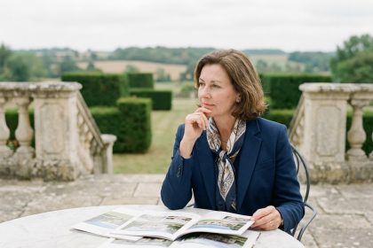 Femme élégante en blazer bleu et foulard regardant des brochures immobilières